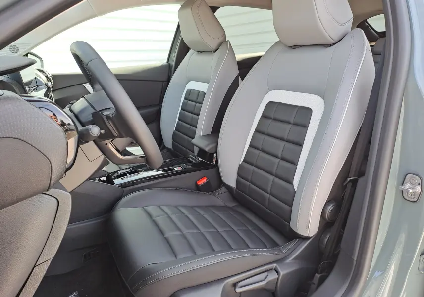Vue intérieure côté conducteur de la CITROEN C4 hybride 2025 avec sièges bicolores gris clair et noir en cuir et tissu.