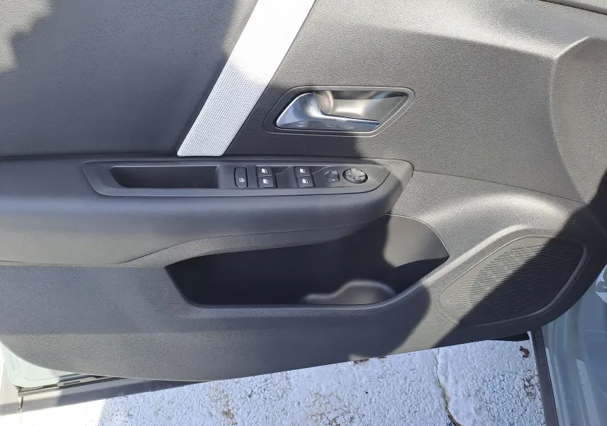 Panneau de porte côté gauche de la Citroën C4 hybride 2025 avec commandes de vitres et poignée argentée.