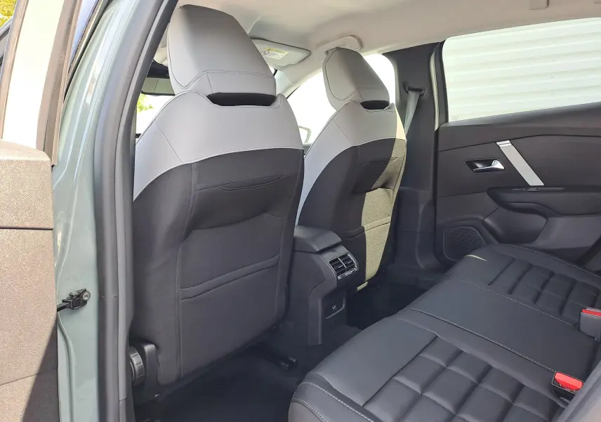 Vue arrière intérieure côté gauche du Citroën C4 hybride 2025 en Manhattan Green, sièges bi-matière gris clair et noir.