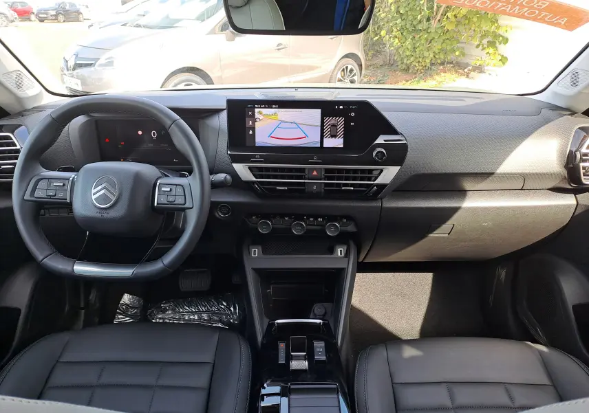 Vue intérieure avant du Citroën C4 hybride 2025 montrant tableau de bord noir avec écran tactile et volant multifonction.