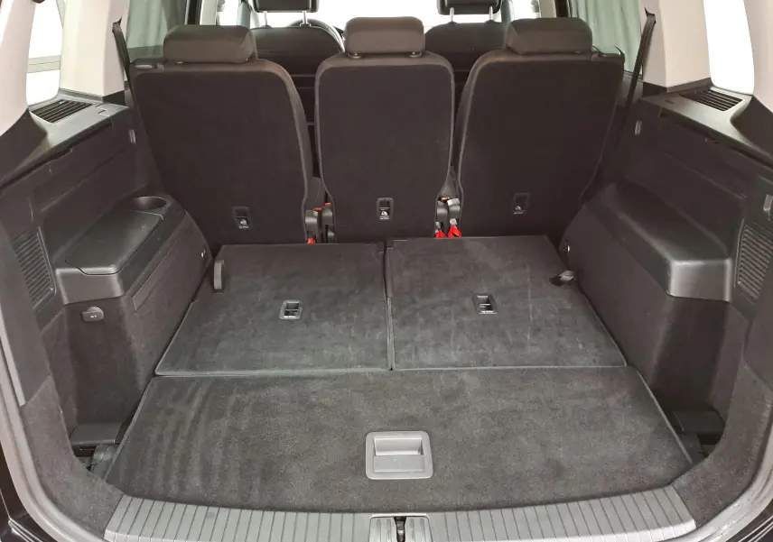 Vue arrière du coffre du Volkswagen Touran 2025 noir Grenadille avec sièges arrière partiellement rabattus et espace de chargement plat.