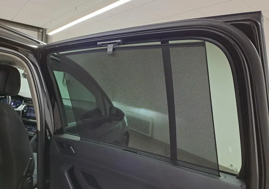 Vue intérieure du côté gauche arrière du Volkswagen Touran noir Grenadille, avec pare-soleil en filet déployé sur la vitre.