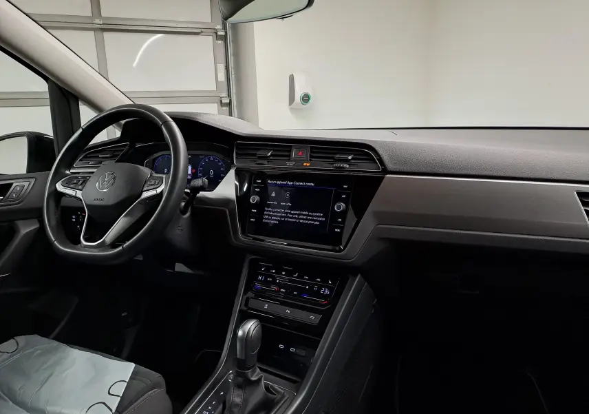 Vue intérieure côté conducteur du Volkswagen Touran 2025, tableau de bord moderne avec écran tactile et volant multifonction noir.