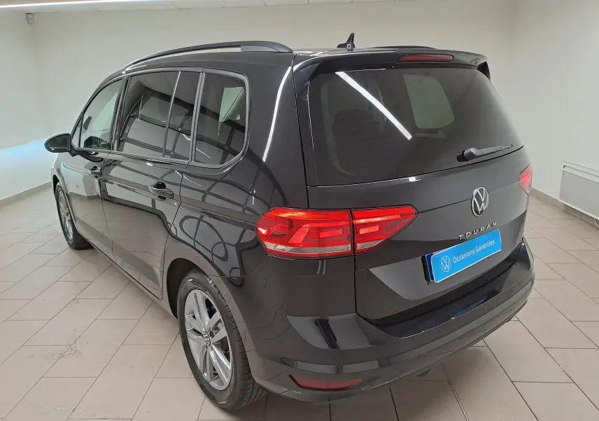 Vue 3/4 arrière droite du Volkswagen Touran noir grenadille 2025, avec feux arrière allumés et vitres teintées.