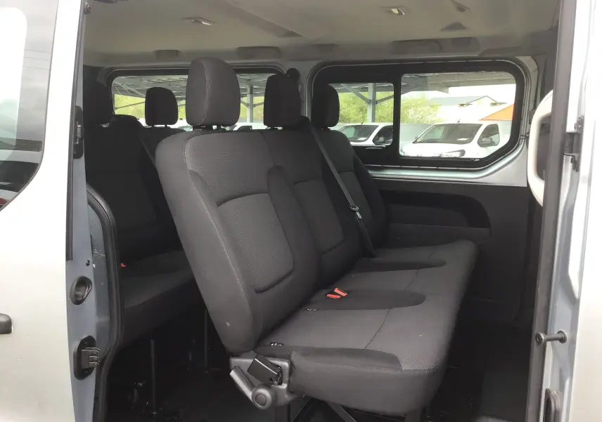 Vue intérieure côté droit sur les sièges noirs du Renault Trafic Combi gris clair, version 9 places avec porte coulissante ouverte.