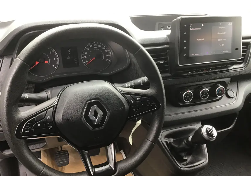 Vue intérieure du poste de conduite du Renault Trafic Combi gris clair, avec volant multifonction et levier de vitesse manuel.