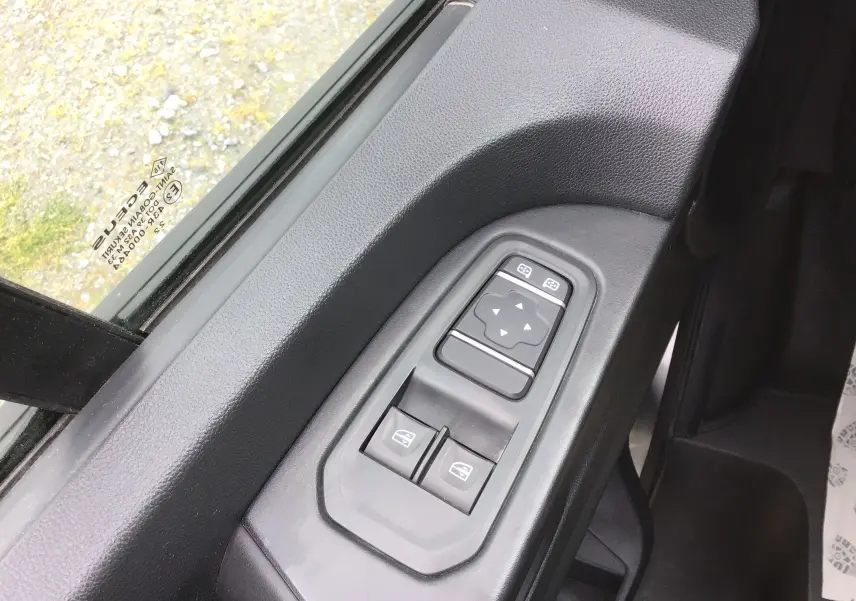 Gros plan sur les commandes de lève-vitres et réglage des rétroviseurs côté conducteur du Renault Trafic Combi gris clair.