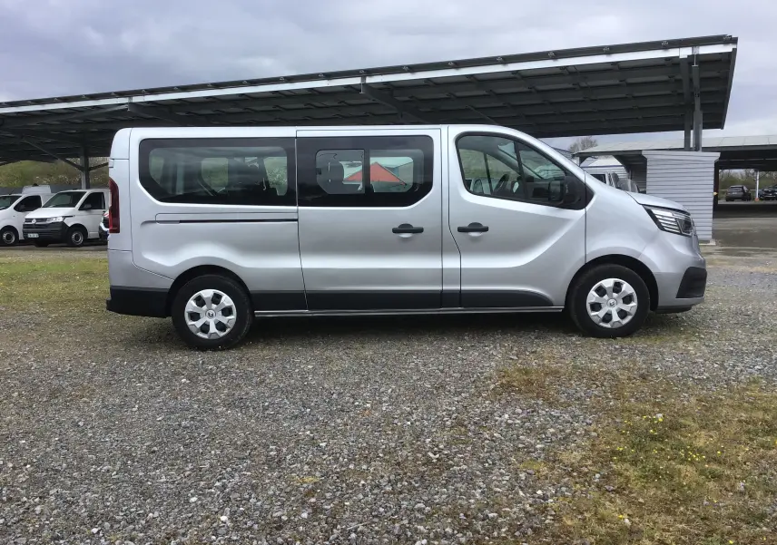 Profil latéral droit d'un Renault Trafic Combi gris clair métallisé, avec fenêtres teintées et jantes acier.