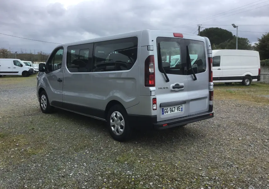 Vue 3/4 arrière droit d’un Renault Trafic Combi gris clair métal, avec vitres latérales teintées et hayon arrière vitré.