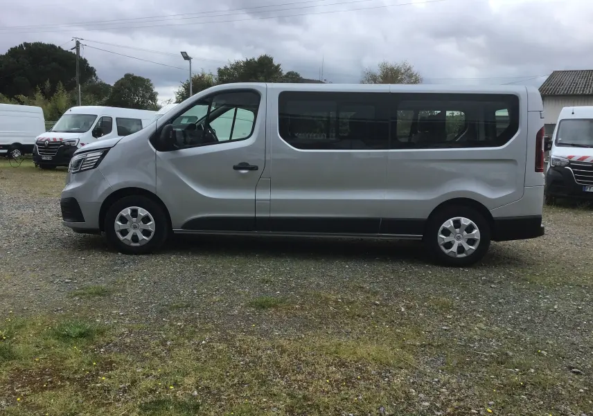 Profil côté gauche d'un Renault Trafic Combi gris clair métal 2022, grand fourgon 9 places avec vitres latérales teintées.