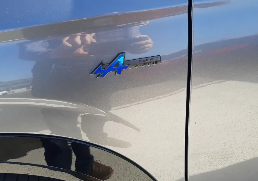 Gros plan sur l'emblème bleu "Esprit Alpine" sur l'aile avant droite du Renault Austral gris schiste avec toit noir.