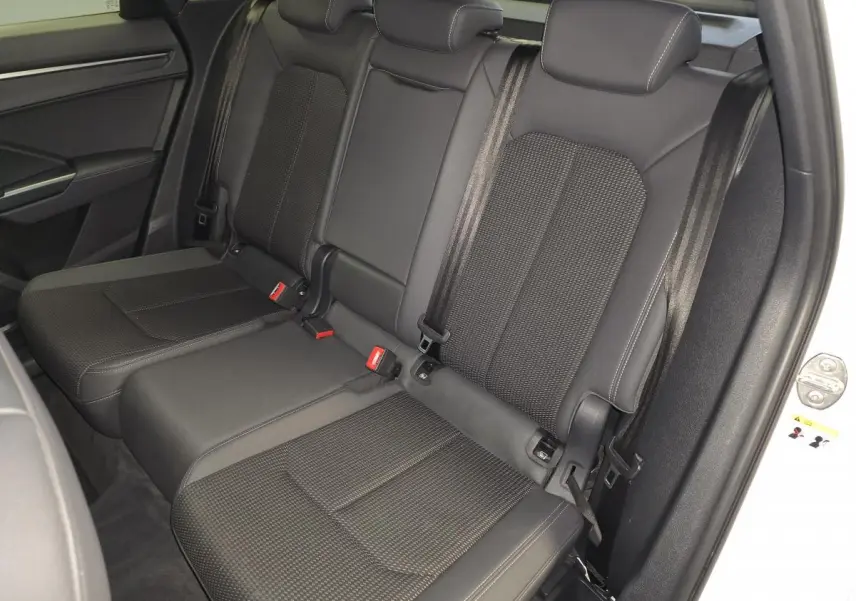 Vue intérieure sur les sièges arrière noirs en cuir et tissu du Audi Q3 blanc, avec ceintures de sécurité visibles.