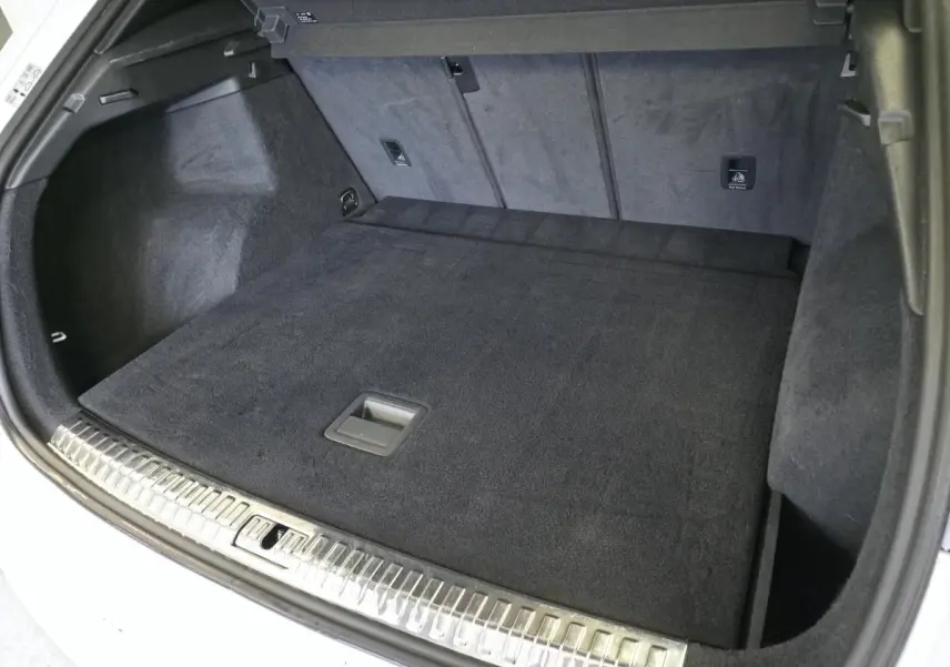 Coffre ouvert vu de l'arrière d'un Audi Q3 blanc, avec tapis de sol noir et seuil de chargement en métal.