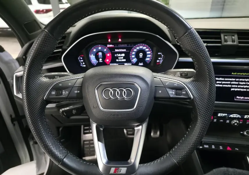 Vue rapprochée du volant sport S line noir perforé et du tableau de bord numérique d'un Audi Q3 2019.