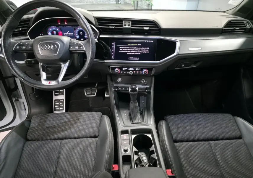 Intérieur Audi Q3 S-Line 2019 vu de face, tableau de bord noir avec écran tactile et volant sport multifonction.