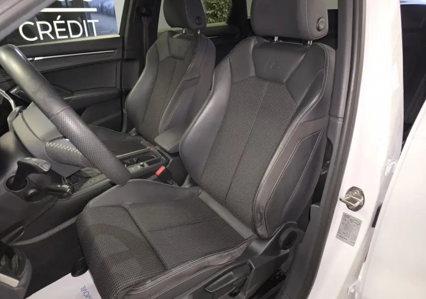 Vue intérieure côté conducteur de l'Audi Q3 blanc, mettant en valeur les sièges sport S line en cuir noir avec logo embossé.
