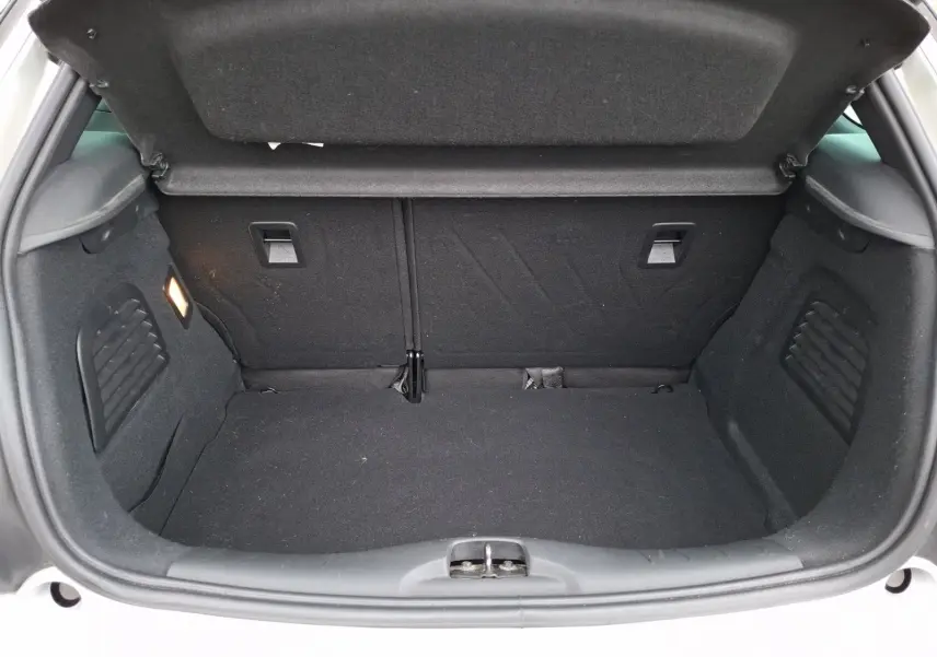Coffre ouvert vu de l’arrière d’une Citroën DS3 gris clair, montrant l’espace de chargement vide et la moquette noire.