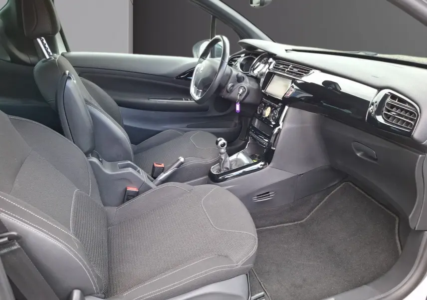 Vue intérieure côté droit de la Citroën DS3 2015 avec sièges gris, tableau de bord noir brillant et boîte manuelle.