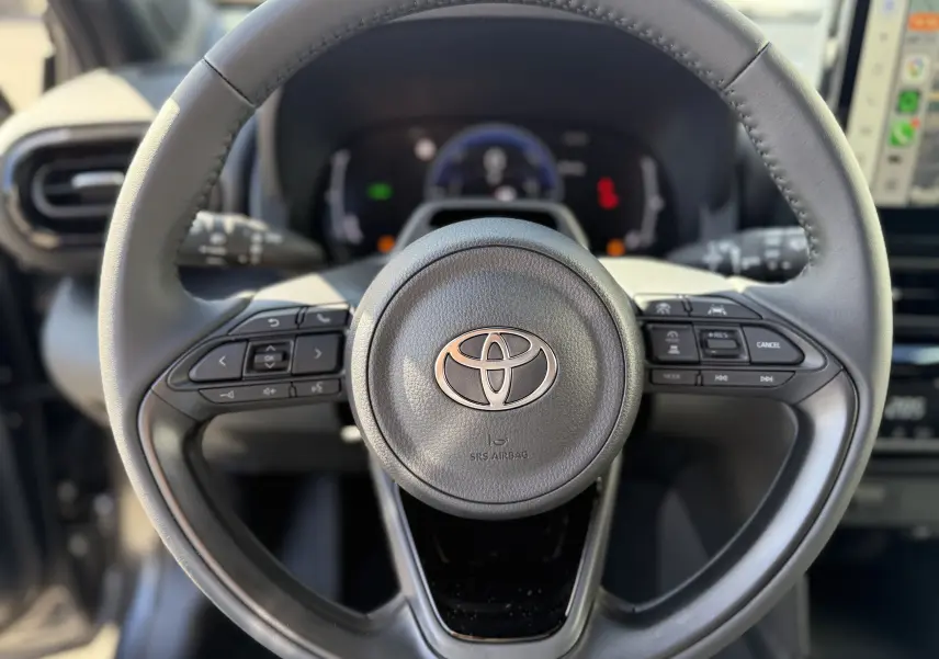 Vue rapprochée du volant noir de la Toyota Yaris Cross 1.5 Hybrid 2026 avec commandes intégrées et logo central argenté.