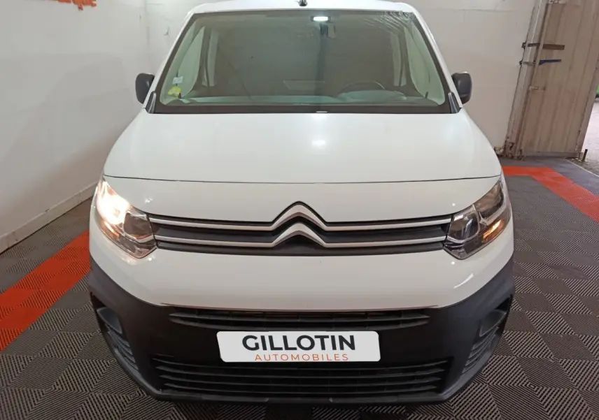 Vue avant d’un Citroën Berlingo blanc 2021 avec phares allumés et pare-chocs noir dans un garage.