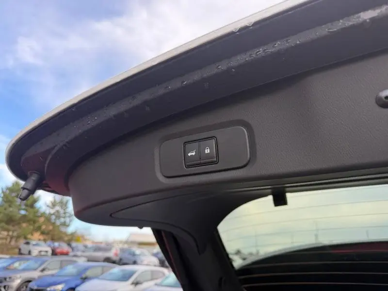 Gros plan sur le bouton d'ouverture et de verrouillage du hayon du Nissan Qashqai blanc nacré, vue intérieure arrière du coffre.