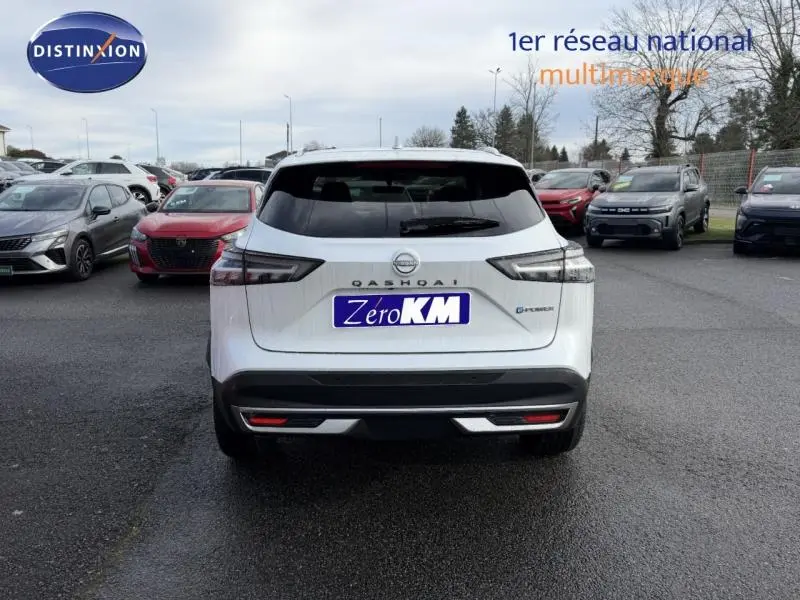 Vue arrière d'un Nissan Qashqai Hybrid e-POWER 2025 en blanc nacré avec logo et badge e-POWER visibles sur un parking.