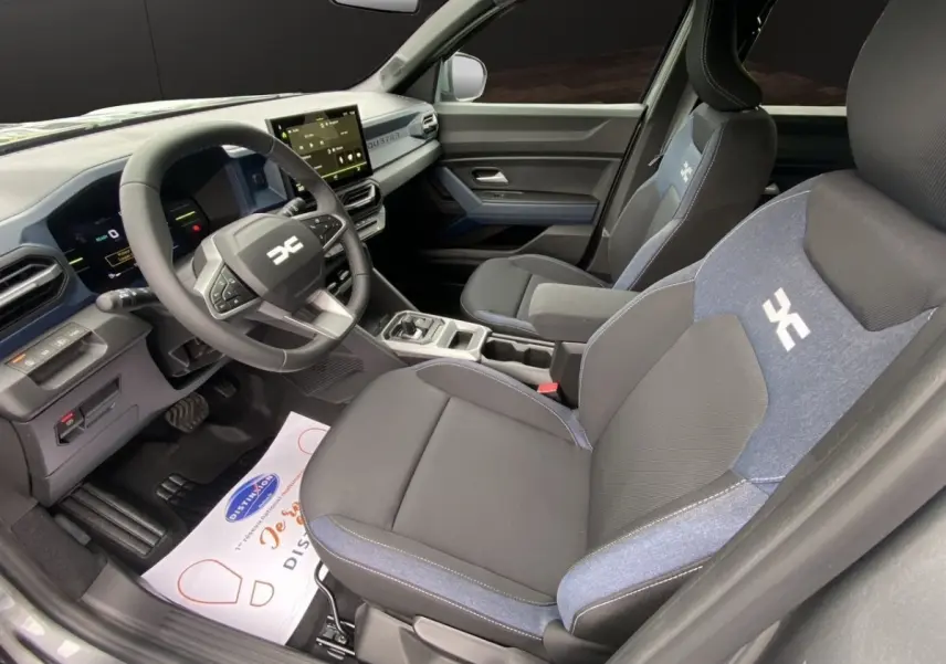 Vue intérieure côté conducteur du Dacia Duster Journey Hybrid 140, sièges noirs avec inserts bleus et tableau de bord moderne.