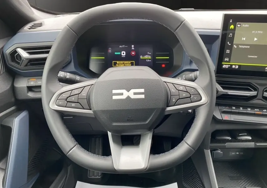 Vue intérieure centrée sur le volant multifonctions et le tableau de bord numérique du Dacia Duster gris foncé.