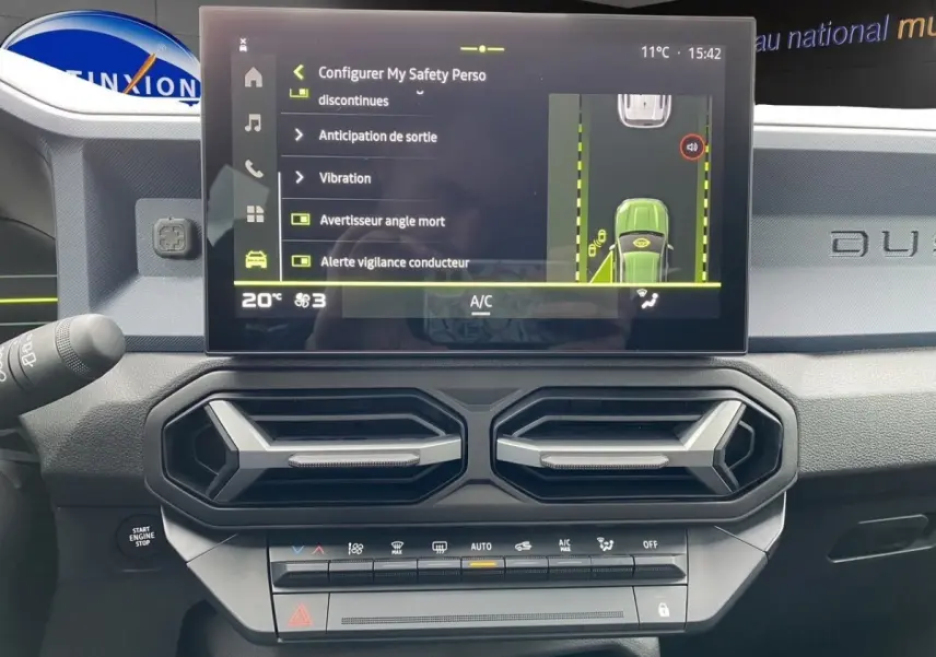 Vue rapprochée de l'écran tactile central et des aérateurs hexagonaux du tableau de bord gris foncé du Dacia Duster 2025.