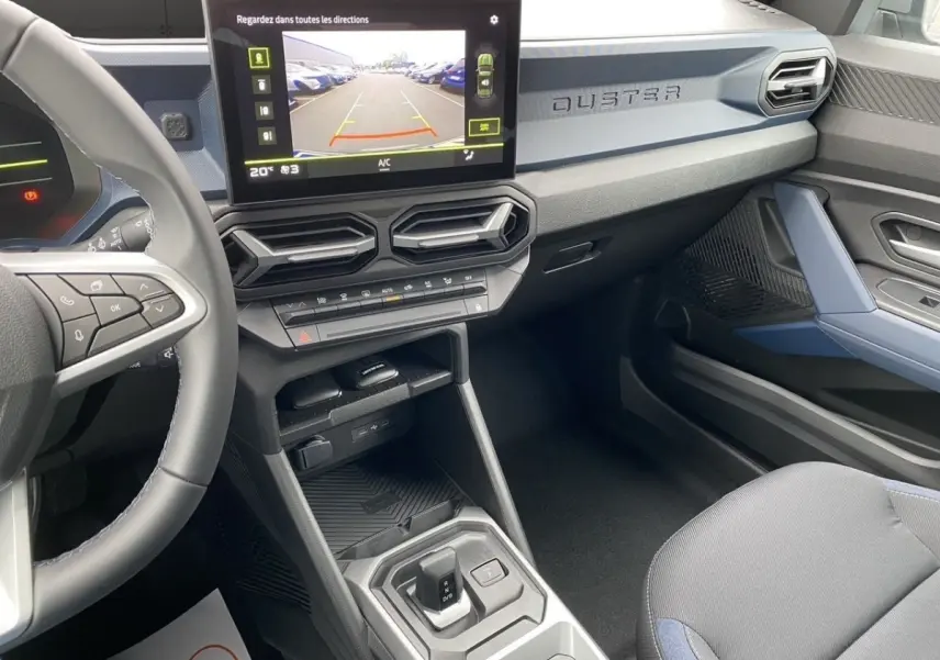 Intérieur du Dacia Duster 2025 gris foncé, vue côté passager avec écran tactile central et volant multifonctions.