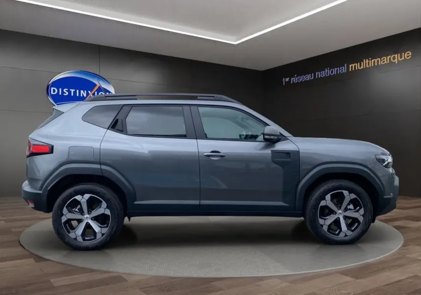 Profil droit du Dacia Duster Journey Hybrid 140 gris foncé avec jantes alliage et barres de toit noires.