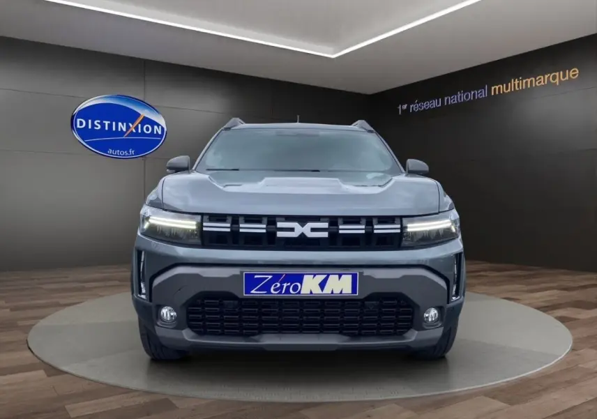 Vue frontale d'un Dacia Duster Journey Hybrid 140 gris foncé avec calandre noire et feux LED allumés.