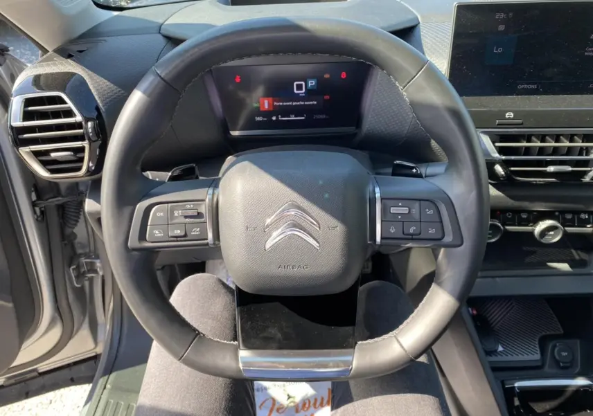 Vue rapprochée du volant de la Citroën C4 2021 gris foncé, avec commandes intégrées et tableau de bord digital.