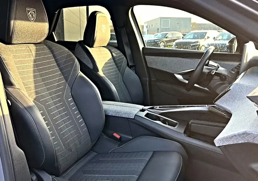 Vue intérieure côté conducteur du Peugeot 3008 gris 2025, sièges tissu et cuir avec logo Peugeot brodé sur appuie-tête.