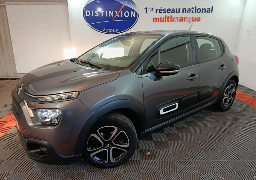 Citroën C3 BlueHDi 100 gris foncé vue 3/4 avant droit avec protections latérales blanches et jantes stylisées.