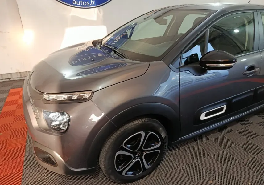 Vue 3/4 avant droit d'une Citroën C3 2024 gris foncé avec jantes alliage et protections latérales blanches.
