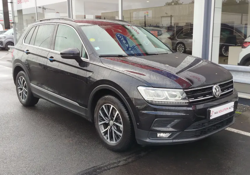 Volkswagen Tiguan 2.0 TDI noir nacré vu en 3/4 avant droit sous la pluie, avec jantes alliage et feux LED.