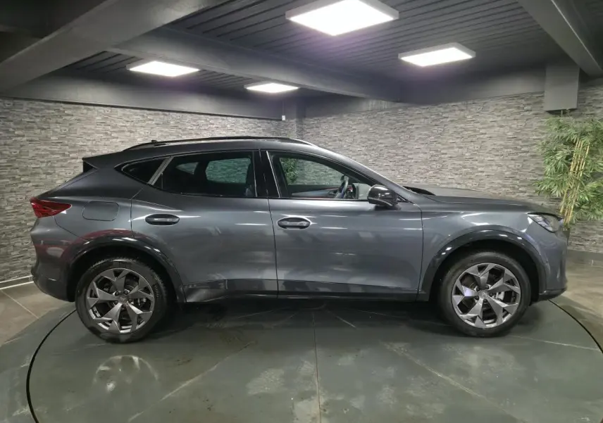 Vue de profil côté gauche d’un CUPRA Formentor gris métallisé avec jantes alliage 18'' et bas de caisse noir obsidien.