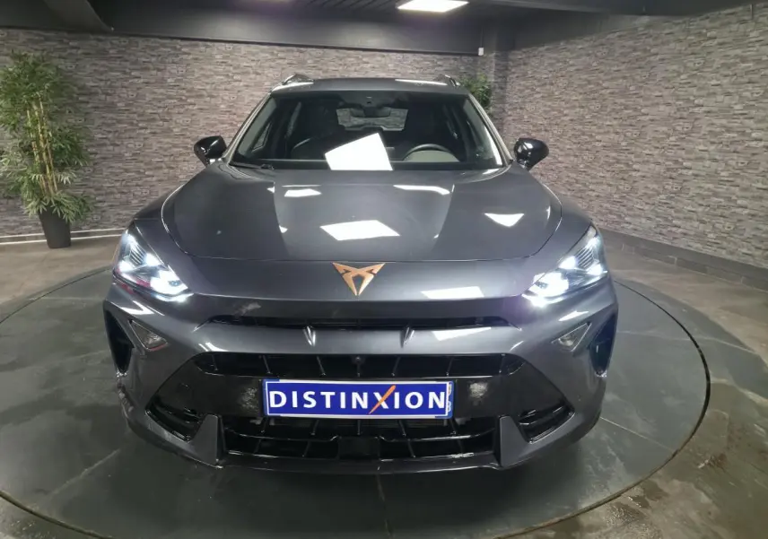 Vue avant d'un CUPRA Formentor gris métallisé avec phares allumés et logo cuivré sur le capot dans un showroom.