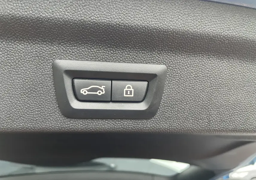 Gros plan sur les boutons d'ouverture de coffre et de verrouillage, sur la garniture intérieure noire du hayon du MINI Countryman bleu.