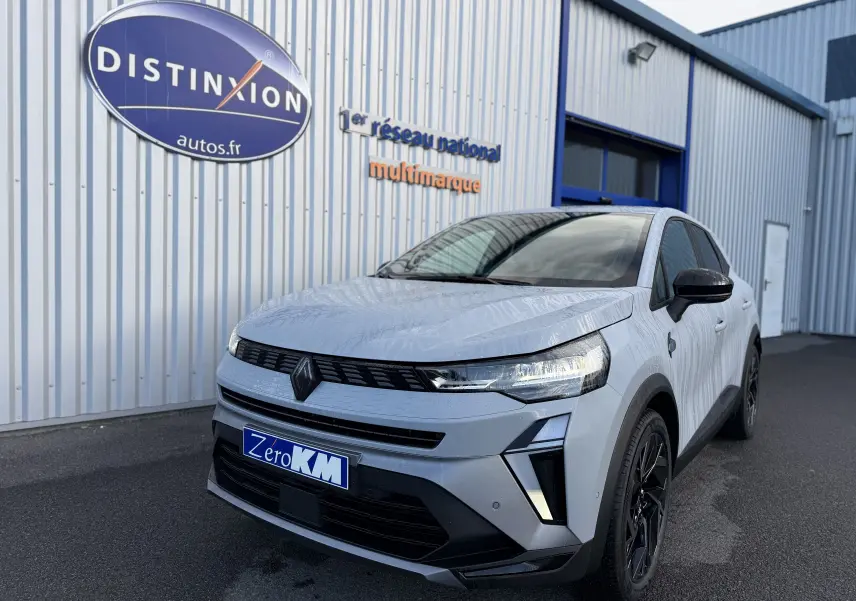Vue 3/4 avant d'une Renault Symbioz gris rafale avec calandre noire et jantes noires devant un bâtiment industriel.