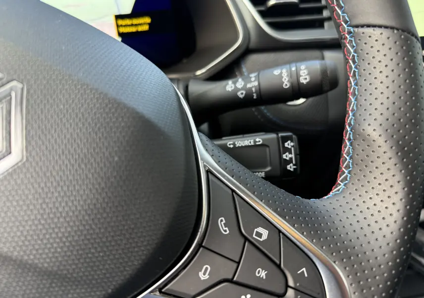 Gros plan sur le volant perforé avec surpiqûres tricolores du Renault Symbioz gris Rafale, affichage numérique en arrière-plan.