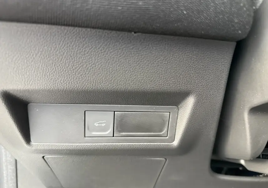 Gros plan sur le bouton d'ouverture du coffre dans l'habitacle du Renault Symbioz gris Rafale, version hybride 2025.