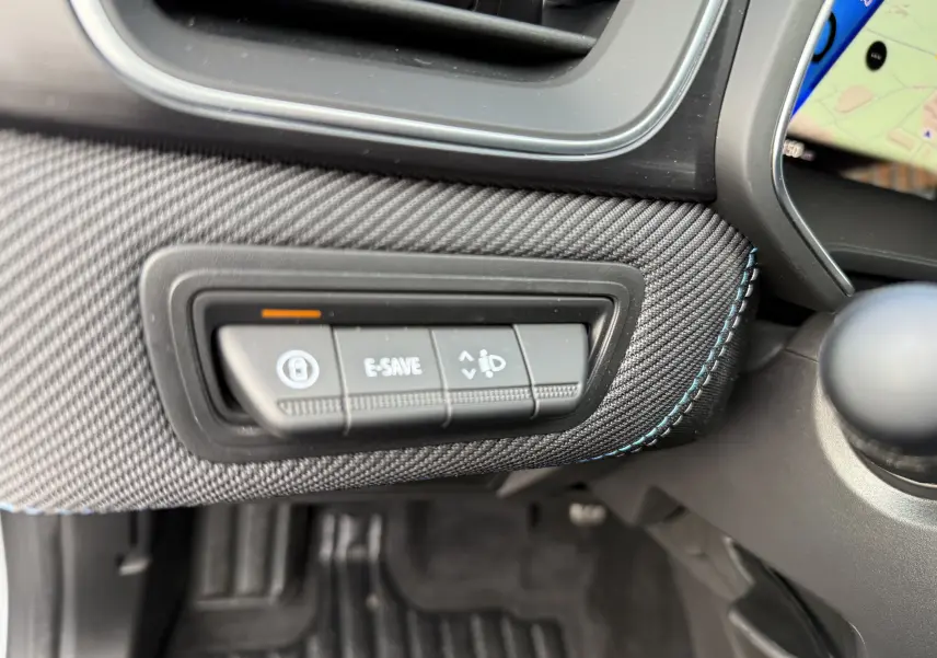 Détail intérieur du tableau de bord du Renault Symbioz 2025, boutons E-SAVE et réglage phares sur habillage gris texturé avec surpiqûres bleues.