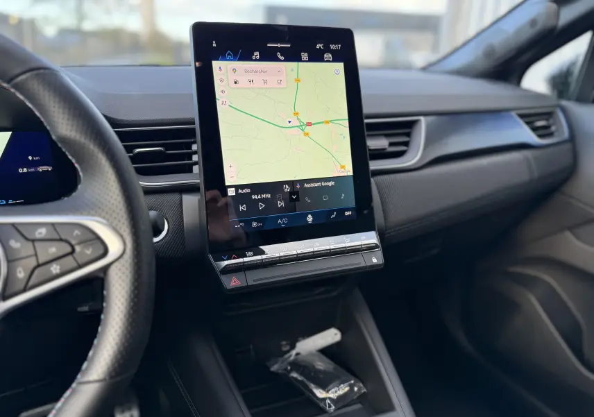 Vue intérieure centrée sur l’écran tactile vertical du tableau de bord de la Renault Symbioz gris Rafale, avec volant partiel à gauche.