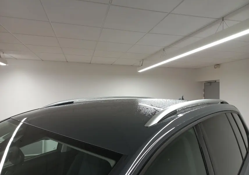 Vue rapprochée du toit gris dauphin métallisé du Volkswagen Touran 2025 avec barres de toit argentées et gouttes d'eau.