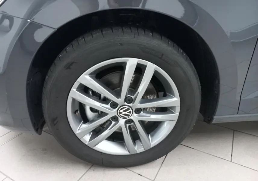 Gros plan sur la roue avant gauche du Volkswagen Touran gris dauphin avec jante alliage à 5 doubles branches.