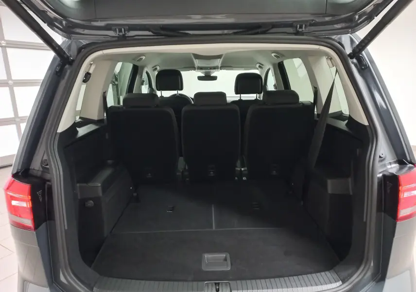 Vue arrière du coffre ouvert du Volkswagen Touran 2025 gris Dauphin, montrant les sièges arrière et l'espace de chargement.