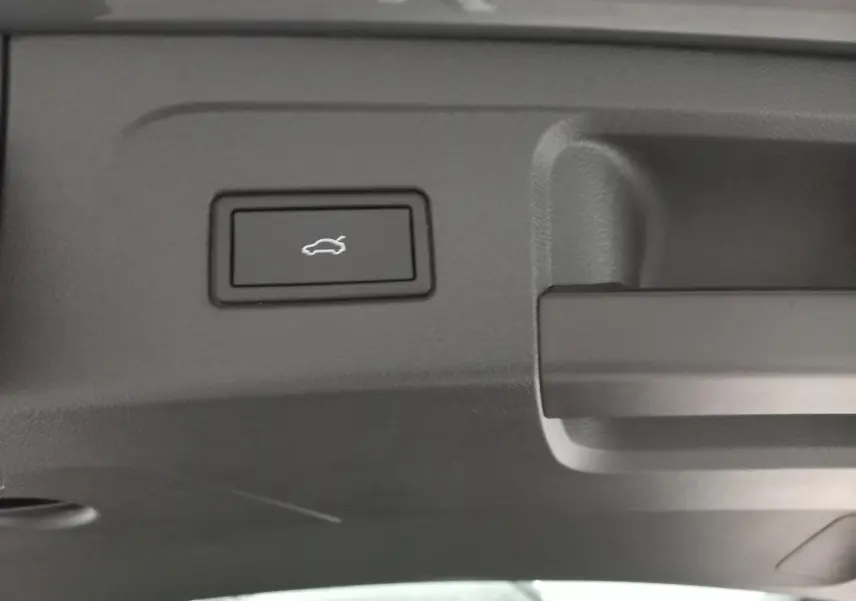 Gros plan sur le bouton d'ouverture électrique du coffre du Volkswagen Touran gris Dauphin, vue intérieure du hayon.