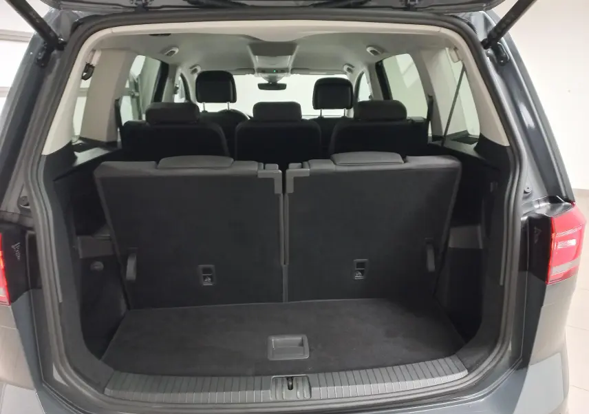 Vue arrière du coffre ouvert du Volkswagen Touran gris dauphin 2025, montrant les trois rangées de sièges rabattables.
